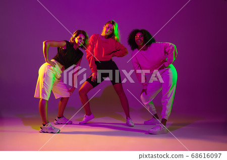 Sportive girls dancing hip-hop in stylish clothes on gradient background at dance hall in neon light 68616097