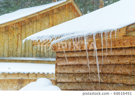 long icicles of ice on the roof of a wooden house in winter with heavy snowfall long icicles of ice on the roof of a wooden house in winter with heavy snowfall 68616491