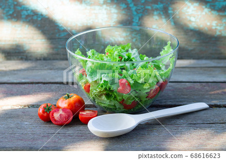 Healthy organic salad with fresh vegetables and herbs in glass bowl with wooden spoon on rustic table 68616623