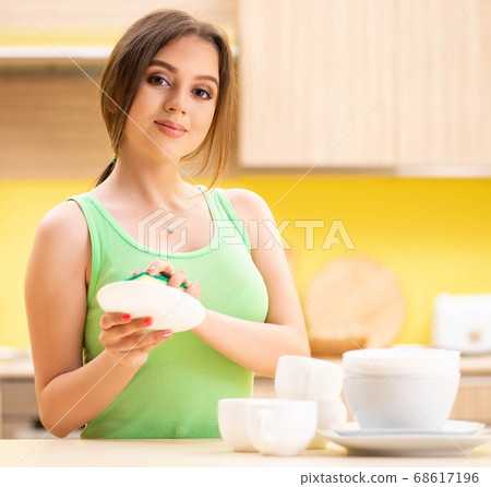 Young woman cleaning and washing dishes in kitchen 68617196
