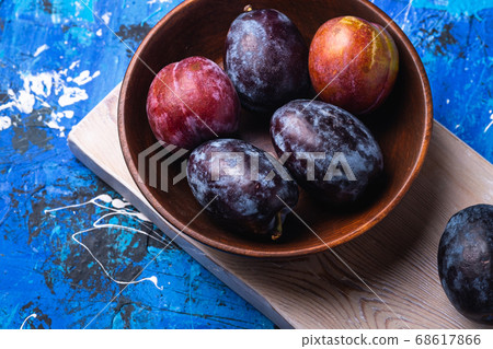 Fresh sweet plum fruits in brown wooden bowl on old cutting board Fresh sweet plum fruits in brown wooden bowl on old cutting board 68617866