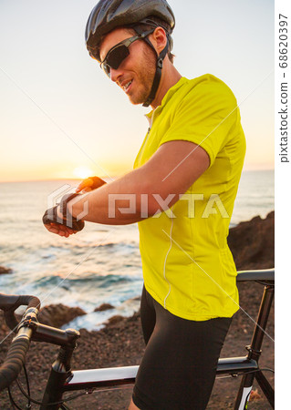Smartwatch biking athlete man cyclist on triathlon race using smart watch on road bike insunset summer outdoor 68620397