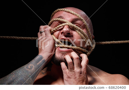 Photo of binded bald man trying tear the rope on face Photo of binded bald man trying tear the rope on face 68620400
