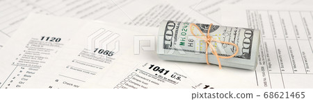 Tax forms lies near roll of hundred dollar bills. 68621465