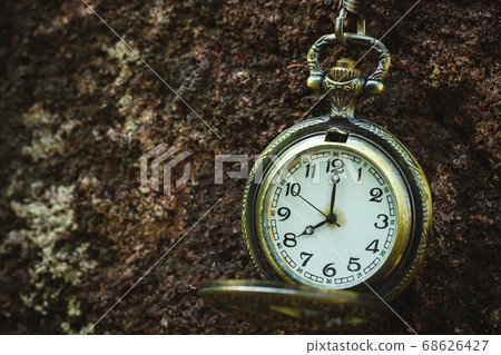 Vintage old pocket watch hanged on the rock background. At 8 o'clock. Closeup and copy space. 68626427
