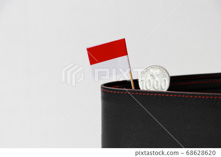 One thousand Rupiah with mini Indonesia flag stick on the black wallet on white background. One thousand Rupiah with mini Indonesia flag stick on the black wallet on white background. 68628620