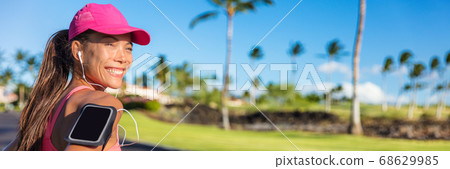 Fitness summer motivation running music woman runner run banner. Jogging Asian girl listening to smartphone app with earphones wearing cap and armband smart phone holder. Horizontal panorama crop 68629985