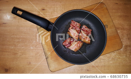 photo of pieces of bacon on a black frying pan on 68630735