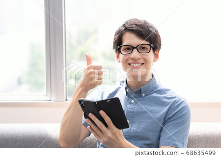 一個男人看著沙發上的智能手機（豎起大拇指） 68635499