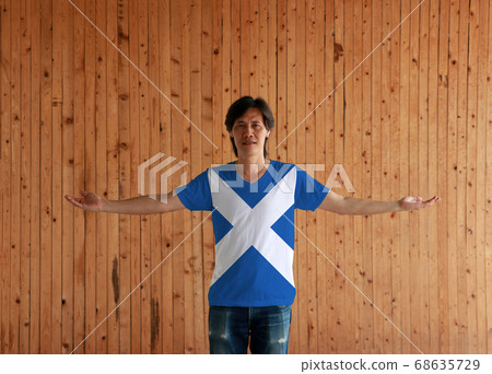 Man wearing Scotland flag color shirt and standing with arms wide open on the wooden wall 68635729