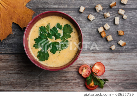 Pumpkin cream soup in bowl with parsley on wooden table with crackers and tomatoes. Traditional autumn food for Halloween Pumpkin cream soup in bowl with parsley on wooden table with crackers and tomatoes. Traditional autumn food for Halloween 68635759
