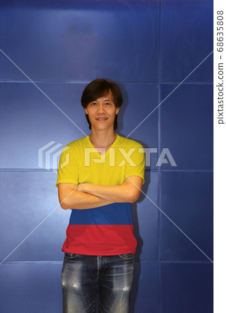 Man wearing Colombia flag pattern shirt and cross one's arm on the blue wall background Man wearing Colombia flag pattern shirt and cross one's arm on the blue wall background 68635808