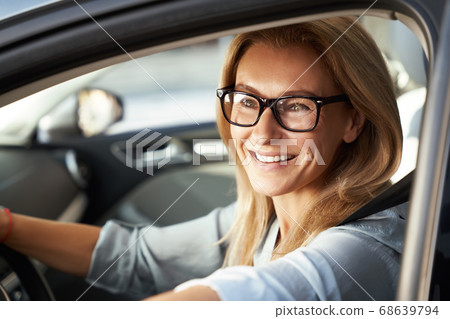 Ready for business trip. Portrait of a beautiful happy caucasian businesswoman wearing glasses sitting in her modern car, looking at camera and smiling 68639794
