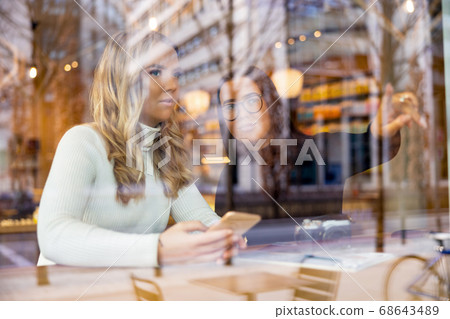 Women Talking and Looking Out Window At Cafe in City 68643489