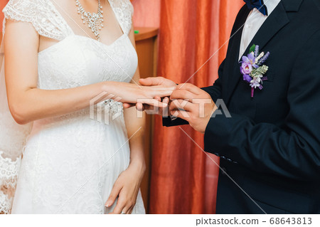groom puts a gold wedding ring on the bride's finger groom puts a gold wedding ring on the bride's finger 68643813