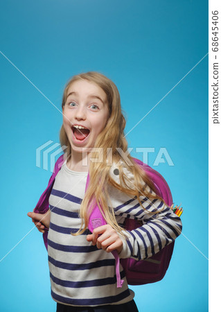 Little Caucasian joyful girl with a school backpack on a blue 68645406