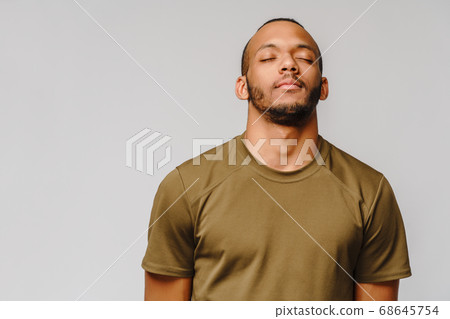 african-american young man in green t-shirt over light grey background with eyes closed with copy space african-american young man in green t-shirt over light grey background with eyes closed with copy space 68645754