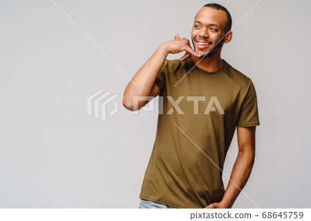 Handsome young African American man showing a call me sign and smiling while standing isolated on grey background Handsome young African American man showing a call me sign and smiling while standing isolated on grey background 68645759