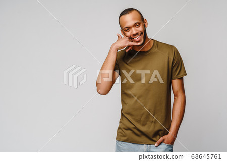 Handsome young African American man showing a call me sign and smiling while standing isolated on grey background Handsome young African American man showing a call me sign and smiling while standing isolated on grey background 68645761
