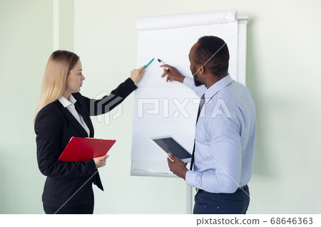 Young businessman working with colleague using flipchart, copyspace 68646363