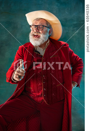Modern stylish Santa Claus in red fashionable suit and cowboy's hat on dark background 68648386