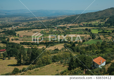 Cottage roof among trees and farmed fields 68650412