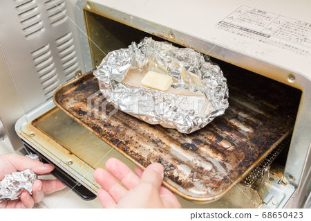 A woman's hand making a foil packet of cod 68650423