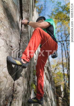 A bearded man aged with a bag of magnesia and rock shoes is trainered on a not high rock in the woods. Training of climbers in natural conditions 68653214