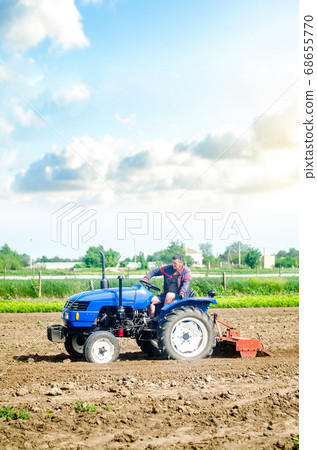The farmer drives a tractor with a milling unit equipment. Loosening land cultivation Use of agricultural machinery to speed up work. Farming. Plowing field. The stage of preparing soil for planting. The farmer drives a tractor with a milling unit equipment. Loosening land cultivation Use of agricultural machinery to speed up work. Farming. Plowing field. The stage of preparing soil for planting. 68655770