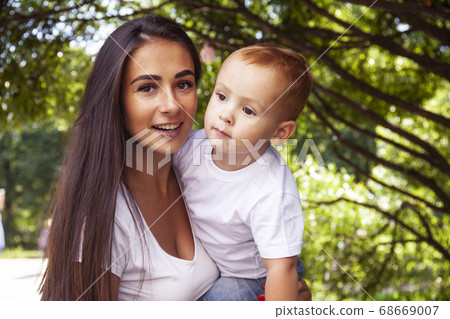 young pretty brunette mother with little cute boy walking in park happy smiling, lifestyle people concept young pretty brunette mother with little cute boy walking in park happy smiling, lifestyle people concept 68669007