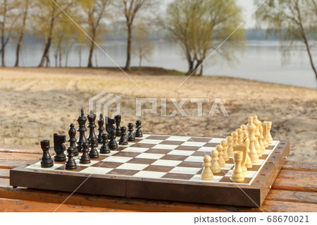 Chess board with chess pieces on bench with river Chess board with chess pieces on bench with river 68670021