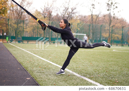 Girl athlete training using trx on sportground. Girl athlete training using trx on sportground. 68670631