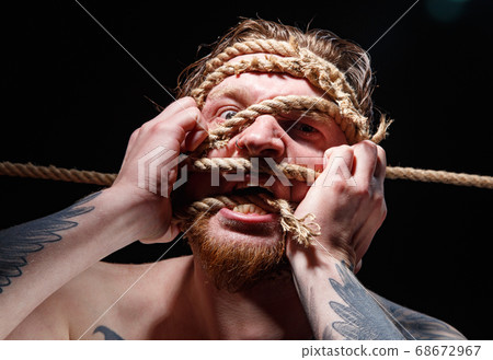 Image of binded tattooed man trying tear the rope on face Image of binded tattooed man trying tear the rope on face 68672967