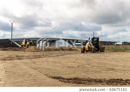 Many heavy heavy industrial road construction machinery on new highway road construction site sunny day with blue sky background. Tipper dumper truck, road-roller and grader machine building freeway Many heavy heavy industrial road construction machinery on new highway road construction site sunny day with blue sky background. Tipper dumper truck, road-roller and grader machine building freeway 68675183