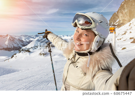 Young adult beautiful happy attractive caucasian smiling skier woman portrait making selfie on mountain peak showing skiing resort panorama breathtaking view. Winter travel adventure welcome concept Young adult beautiful happy attractive caucasian smiling skier woman portrait making selfie on mountain peak showing skiing resort panorama breathtaking view. Winter travel adventure welcome concept 68675447