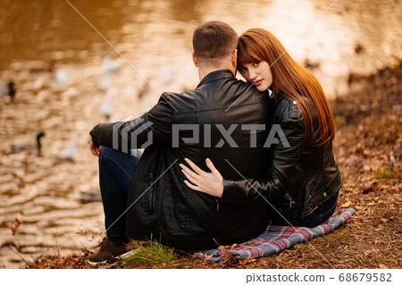 couple sitting on Bank of river in autumn park. 68679582