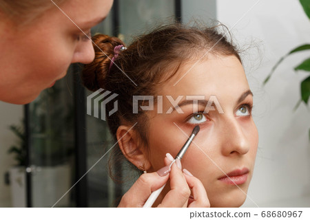 The process of creating makeup. Makeup artist working with a brush on the face of the model. 68680967