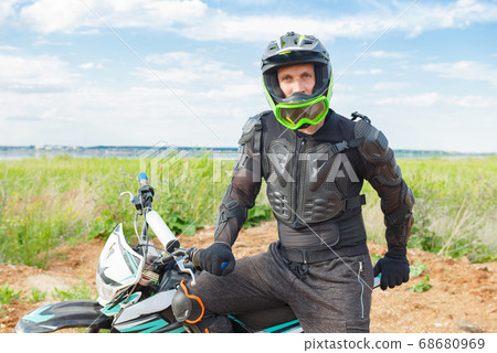A man in motorcycle equipment sits on an enduro motorcycle. 68680969