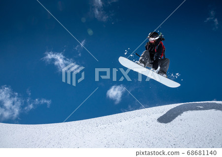 A professional snowboarder girl in flight after jumping from a snow eaves makes a rake against blue sky in sunny day. The concept of winter sports freeride and freestyle A professional snowboarder girl in flight after jumping from a snow eaves makes a rake against blue sky in sunny day. The concept of winter sports freeride and freestyle 68681140
