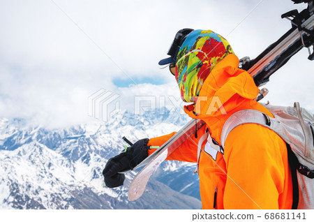 Portrait of a stern climber skier in sunglasses and a cap with a ski mask on his face. holds his skis on his shoulder and looks away against the backdrop of Mount Elbrus 68681141