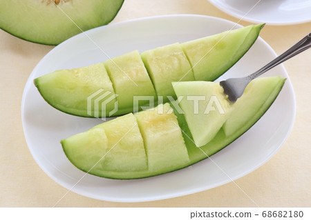 Oval white plate with 2 pieces of cut melon and fork beige back 68682180