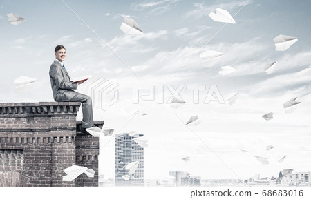 Man on roof edge reading book and cityscape at background Man on roof edge reading book and cityscape at background 68683016