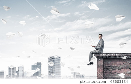 Man on roof edge reading book and cityscape at background Man on roof edge reading book and cityscape at background 68683184