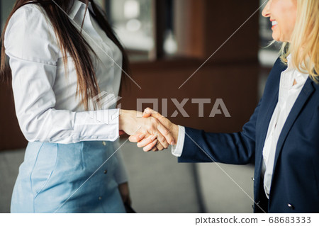 Two businesswomen shaking hands as they close a partnership, focus on hands Two businesswomen shaking hands as they close a partnership, focus on hands 68683333