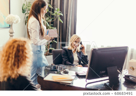 blonde female supervisor talking on phone and meeting in office with coworkers 68683491