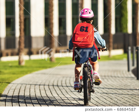 Rear view of a schoolgirl riding a bicycle to 68684587