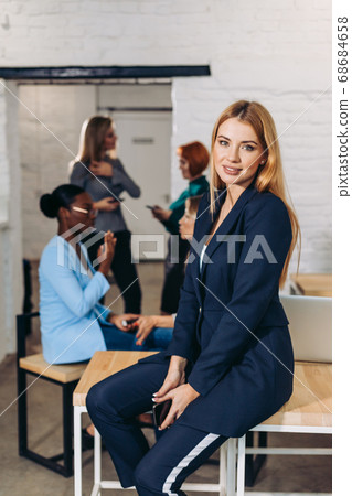 Blonde business woman smiles at camera with colleagues working in background Blonde business woman smiles at camera with colleagues working in background 68684658