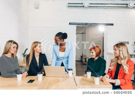 African female boss telling off her female employees, sitting in meeting room. 68684698
