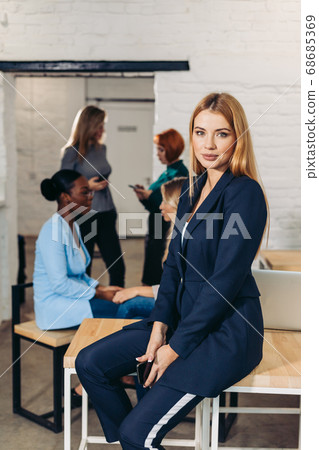 Blonde business woman smiles at camera with colleagues working in background Blonde business woman smiles at camera with colleagues working in background 68685369