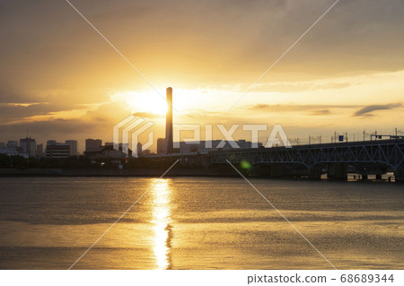 Nishi Kasai, Edogawa Ward, a waste treatment plant and cityscape in front of the Arakawa River illuminated by the setting sun 68689344